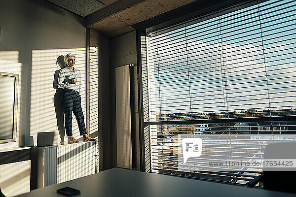 Businesswoman with hand in pocket standing on sideboard in office enjoying the sun