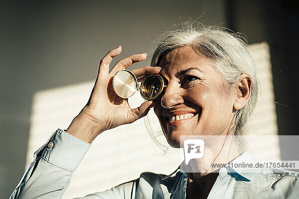 Smiling businesswoman covering eye with navigational compass in office