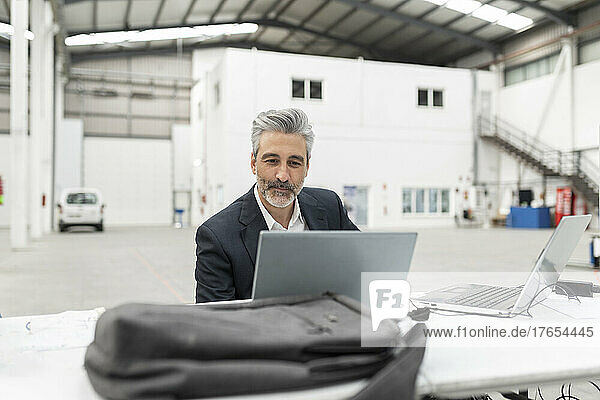 Businessman with laptop sitting at desk in factory