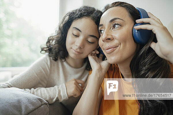Smiling woman listening music through headphones by daughter at home