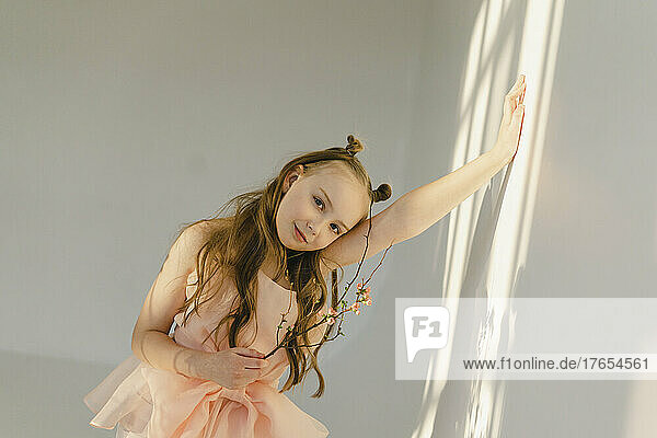 Smiling girl with twig leaning on white wall