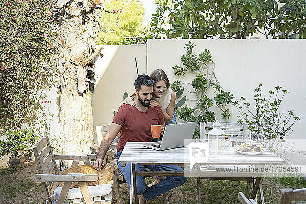 Man using laptop with woman standing behind in back yard