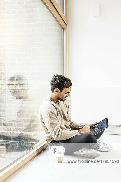 Man using tablet PC sitting cross-legged at home