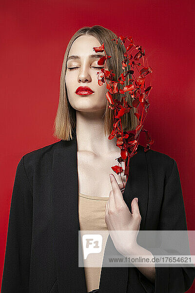 Schöne Frau mit geschlossenen Augen hält einen Zweig vor rotem Hintergrund