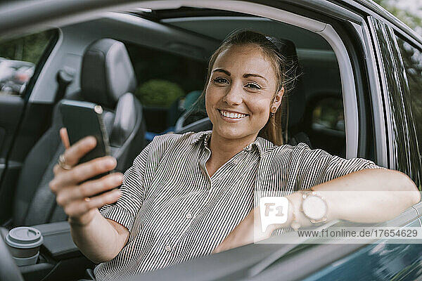Glückliche Frau mit Smartphone sitzt auf dem Fahrersitz im Auto