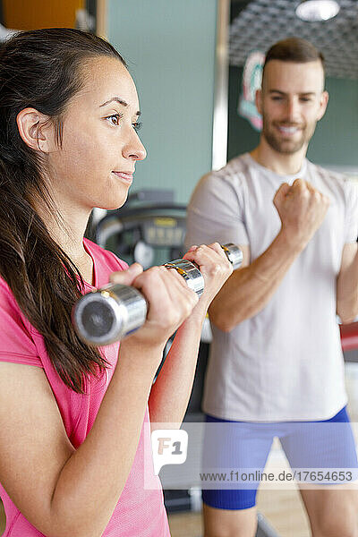 Instructor motivating woman exercising with dumbbells at gym