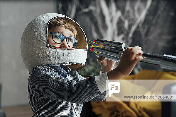 Boy wearing space helmet playing with toy rocket at home