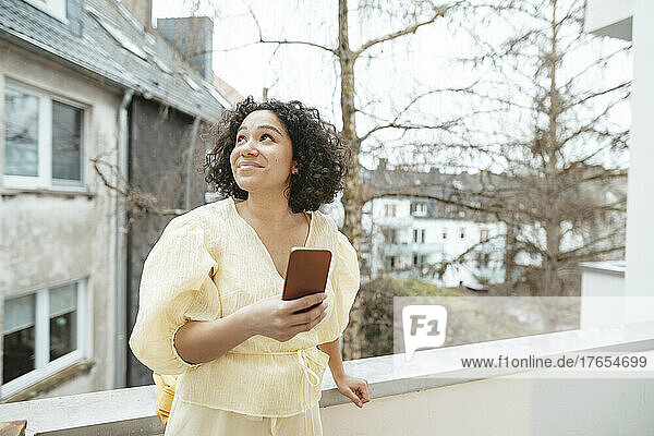 Smiling woman with smart phone standing on balcony