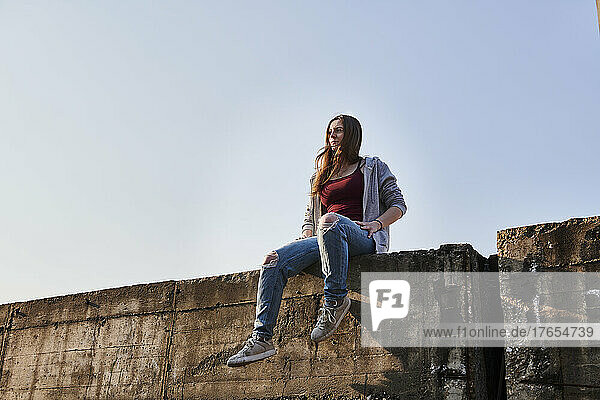 Young woman sitting on concrete wall looking at distance