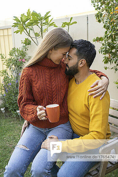 Woman with coffee cup sitting on man's lap in garden