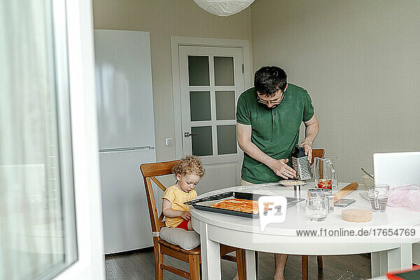 Man making pizza by daughter sitting on chair in kitchen