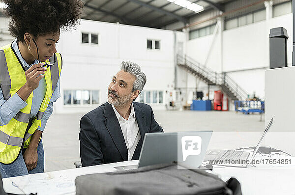 Businessman with laptop discussing with technician at desk in factory