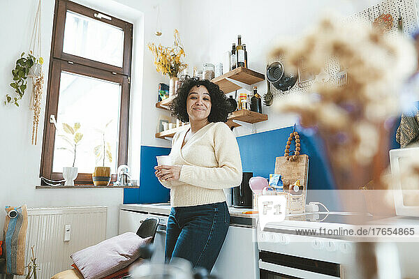 Smiling woman holding coffee cup standing in kitchen at home