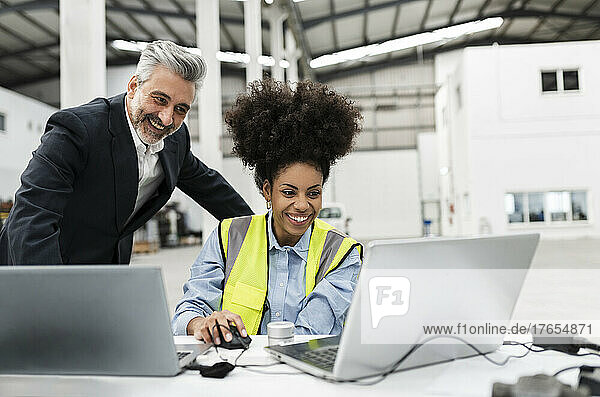 Happy businessman with engineer having video call on laptop in factory