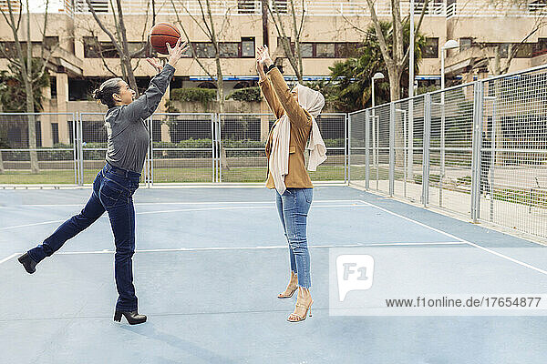 Businesswoman throwing basketball to colleague jumping at sports court
