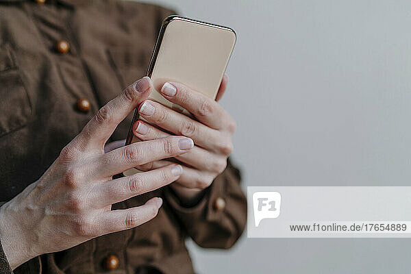 Hand of woman holding mobile phone against gray background