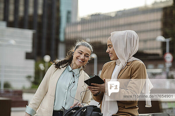 Happy young businesswoman with tablet PC looking at colleague enjoying at office park