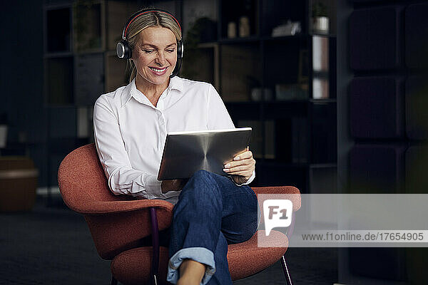 Lächelnde Geschäftsfrau mit Headset und Tablet-PC sitzt auf einem Stuhl