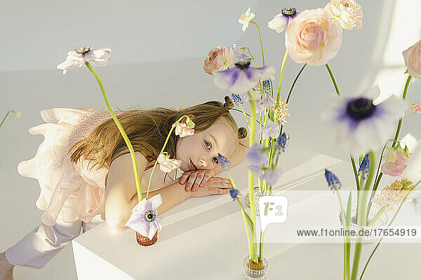 Cute girl leaning on table by flowers in front of white wall