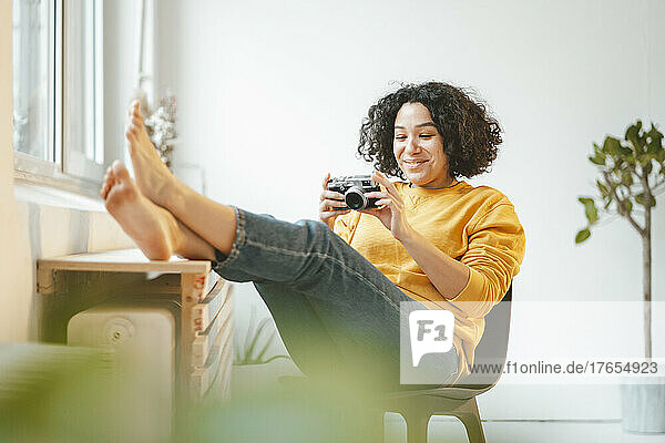 Smiling woman with camera sitting on chair at home
