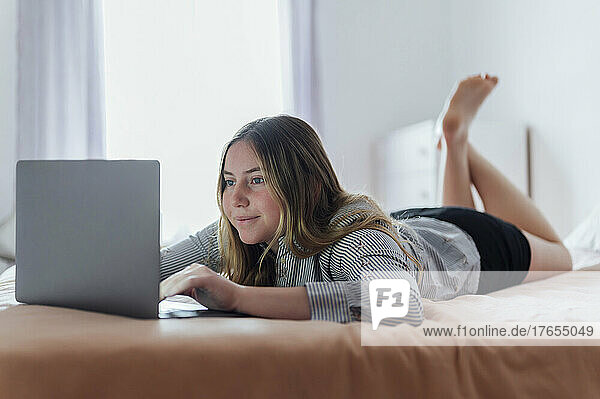 Lächelnde Frau mit Laptop  die zu Hause im Bett liegt
