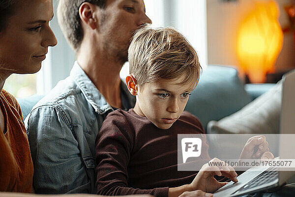 Blond boy using laptop sitting with parents at home