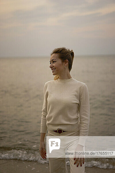 Smiling young beautiful woman standing in front of Baltic sea at sunset