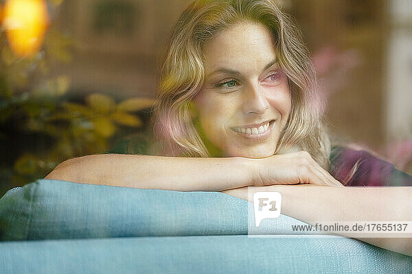 Beautiful smiling woman with blond hair leaning on sofa at home