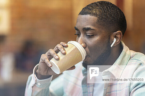 Man drinking coffee through disposable cup in cafe