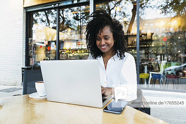 Glückliche Geschäftsfrau sitzt mit Laptop im Straßencafé