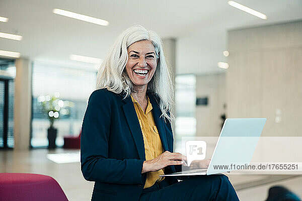 Laughing businesswoman with laptop sitting in office