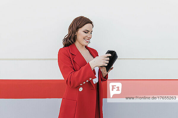 Happy businesswoman using mobile phone standing in front of wall