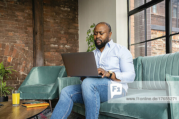 Businessman working sitting on sofa using laptop at office