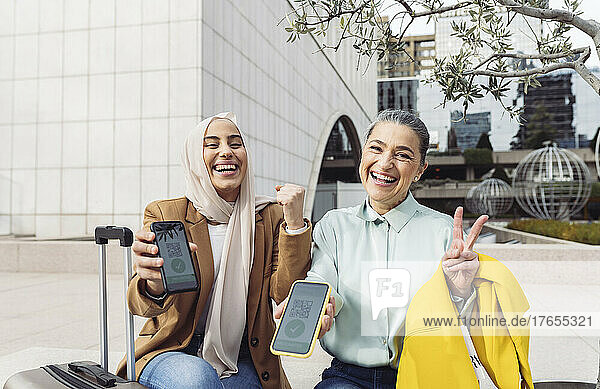 Happy businesswomen gesturing showing vaccination QR certificate on smart phones