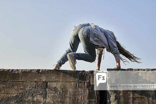 Young woman jumping over concrete wall  rear view