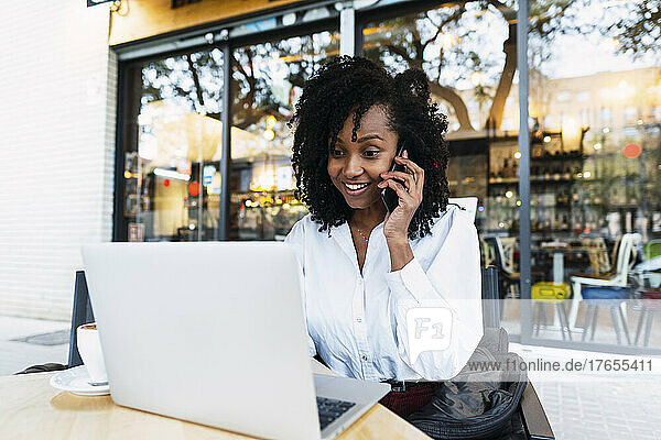 Glückliche Geschäftsfrau mit Laptop und Handy im Straßencafé