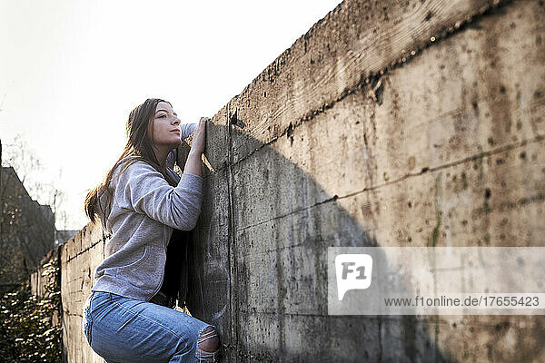 Curious young woman looking over concrete wall