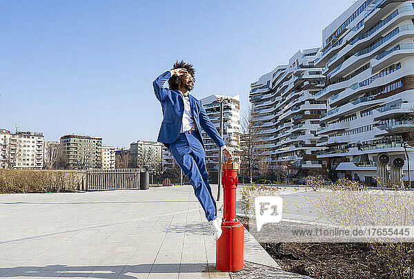 Businessman shielding eyes standing on fire hydrant under clear sky