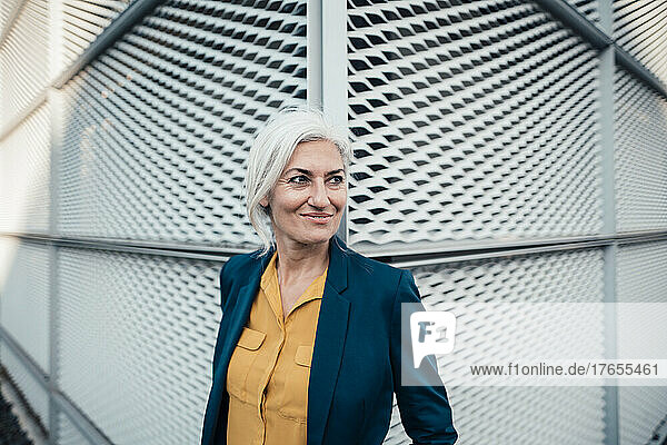 Smiling businesswoman with gray hair standing in front of wall