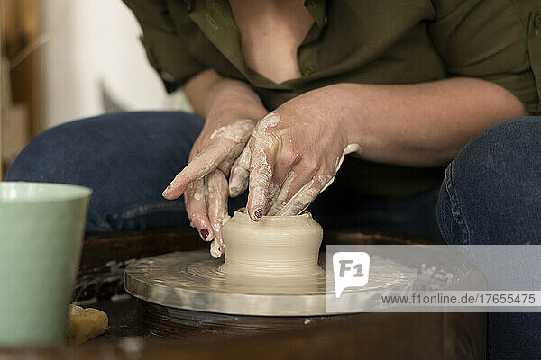 Hands of woman making pot with clay on pottery wheel at workshop