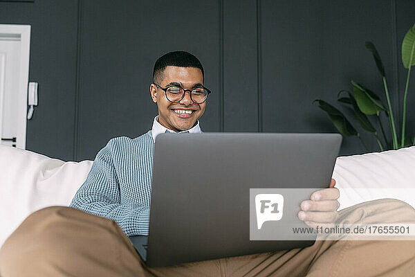 Happy freelancer using laptop sitting on sofa at home
