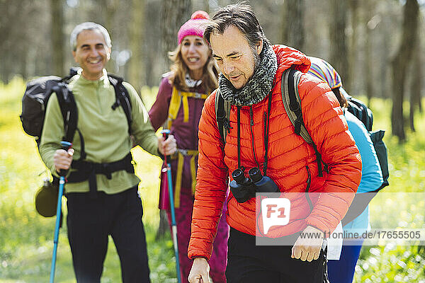 Man wearing binoculars trekking with friends in forest