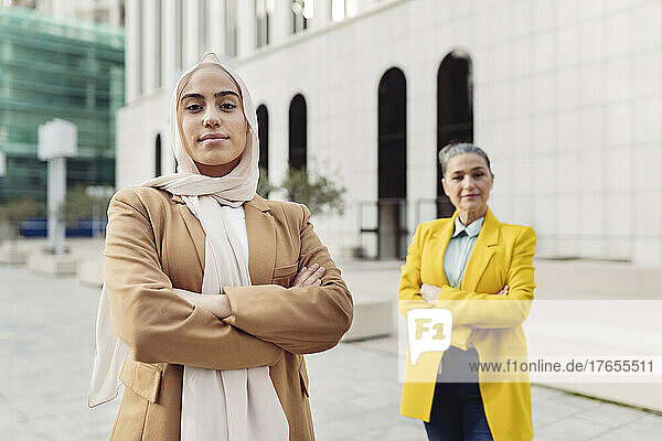 Confident young businesswoman standing with arms crossed in front of colleague at office park