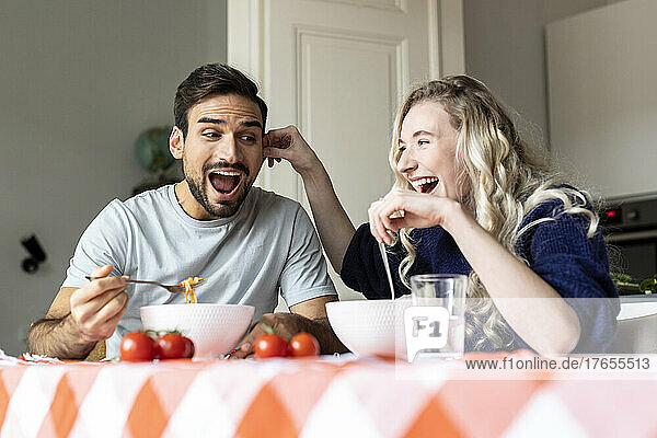 Playful couple eating food on dining table at home