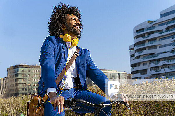Glücklicher Geschäftsmann mit Kopfhörern und Umhängetasche  der Fahrrad fährt