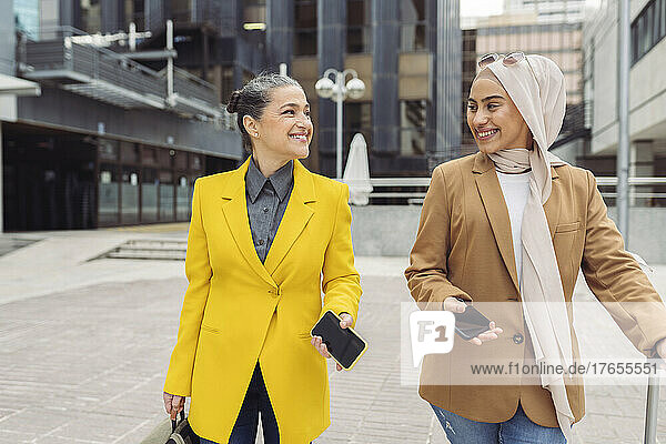 Happy businesswomen with smart phones walking outside modern building