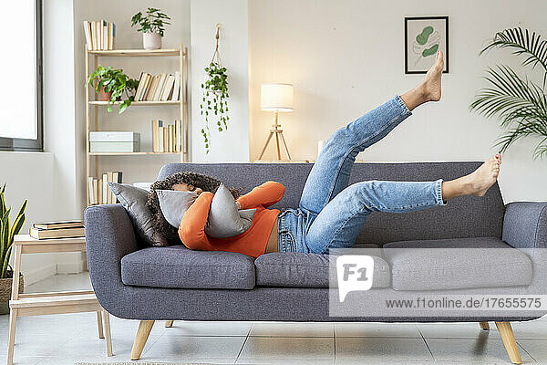 Young woman hugging pillow lying on sofa in living room at home