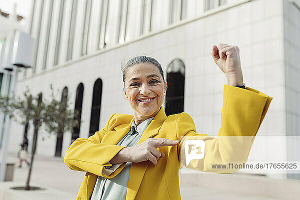 Smiling businesswoman flexing muscle at office park on sunny day
