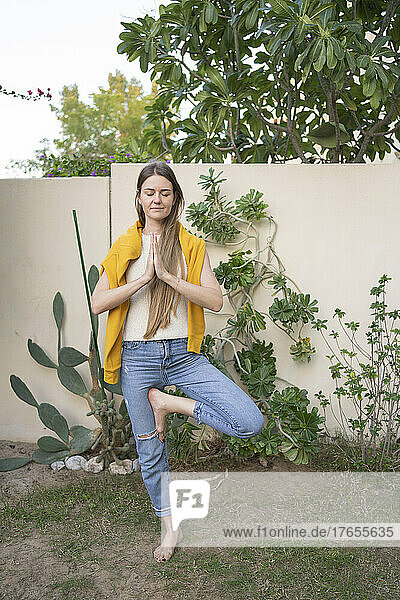 Frau macht Baumpose-Yoga im Garten