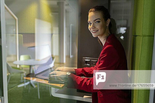 Lächelnde Geschäftsfrau mit Laptop in schallisolierter Kabine im Büro